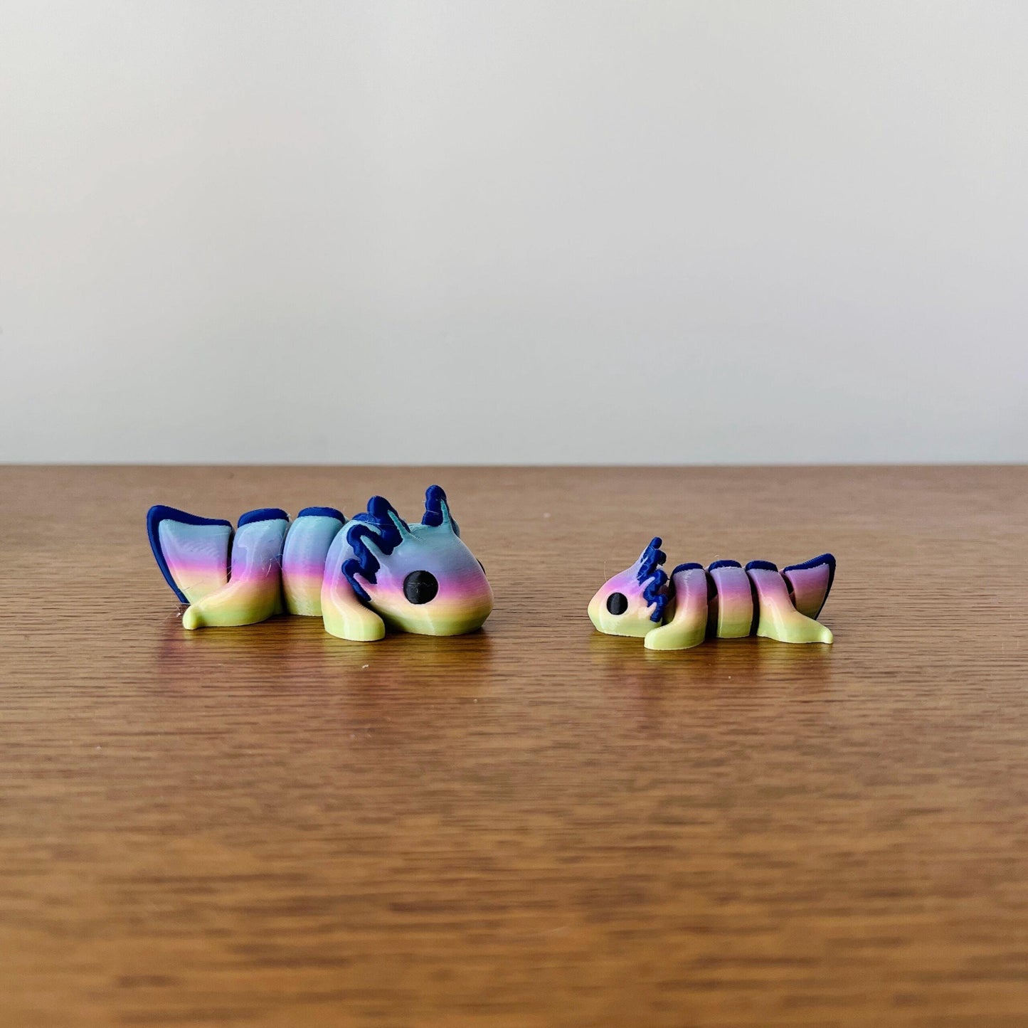 Colorful mini axolotls in vibrant rainbow hues, featuring articulated bodies on a wooden surface.