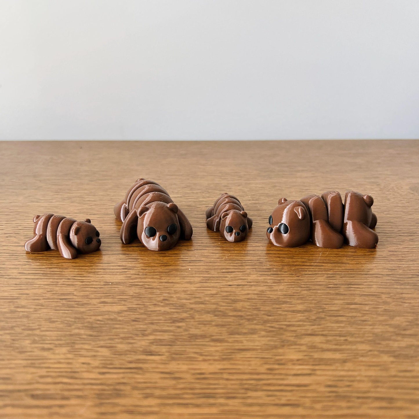 Four adorable mini brown bears in varying sizes, each with black eyes, arranged on a wooden surface.