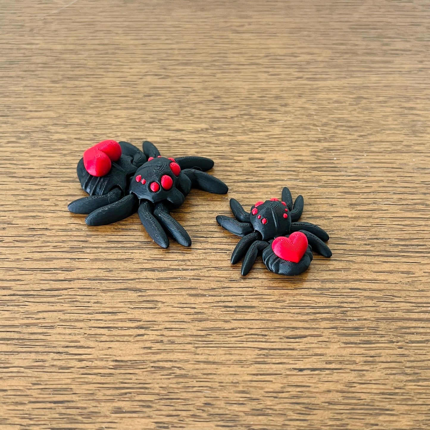 A pair of black spiders with red accents and hearts, showcasing a charming and playful fidget design.