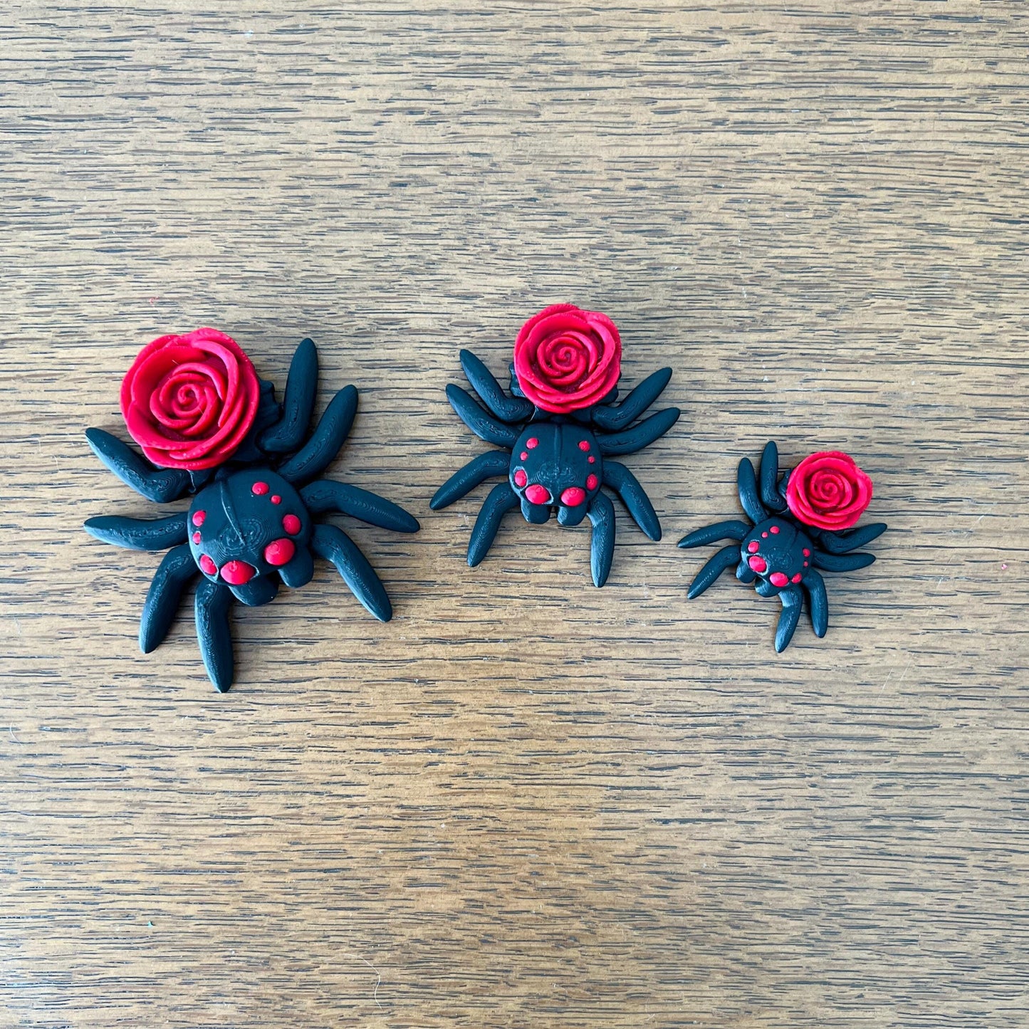 Three black spiders with red rose accents, showcasing a blend of gothic charm and playful elegance.