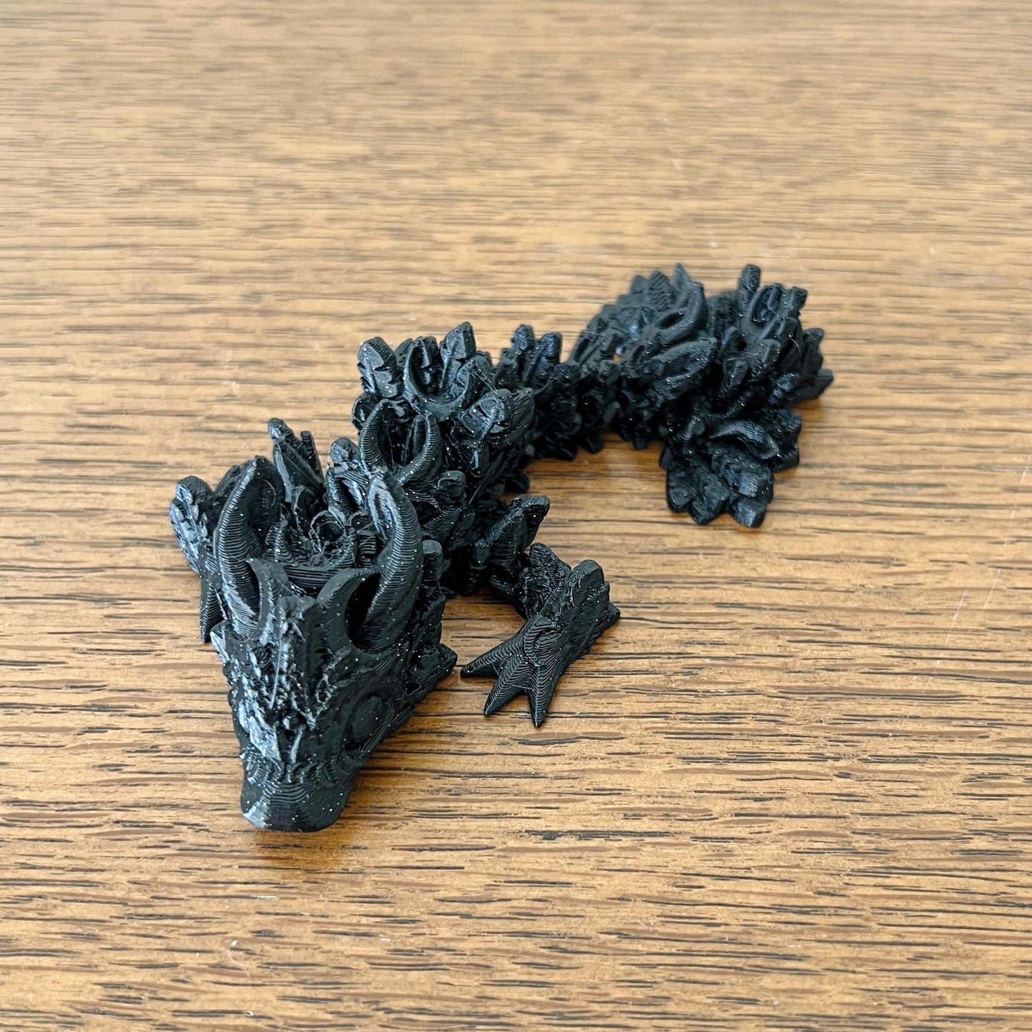 Petite black dragon with intricate lunar-inspired details, resting on a wooden surface, evoking the night sky's magic.
