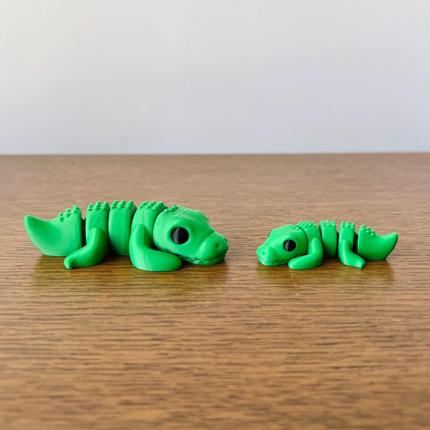 Two vibrant green crocodile figures, one large and one small, resting side by side on a wooden surface.