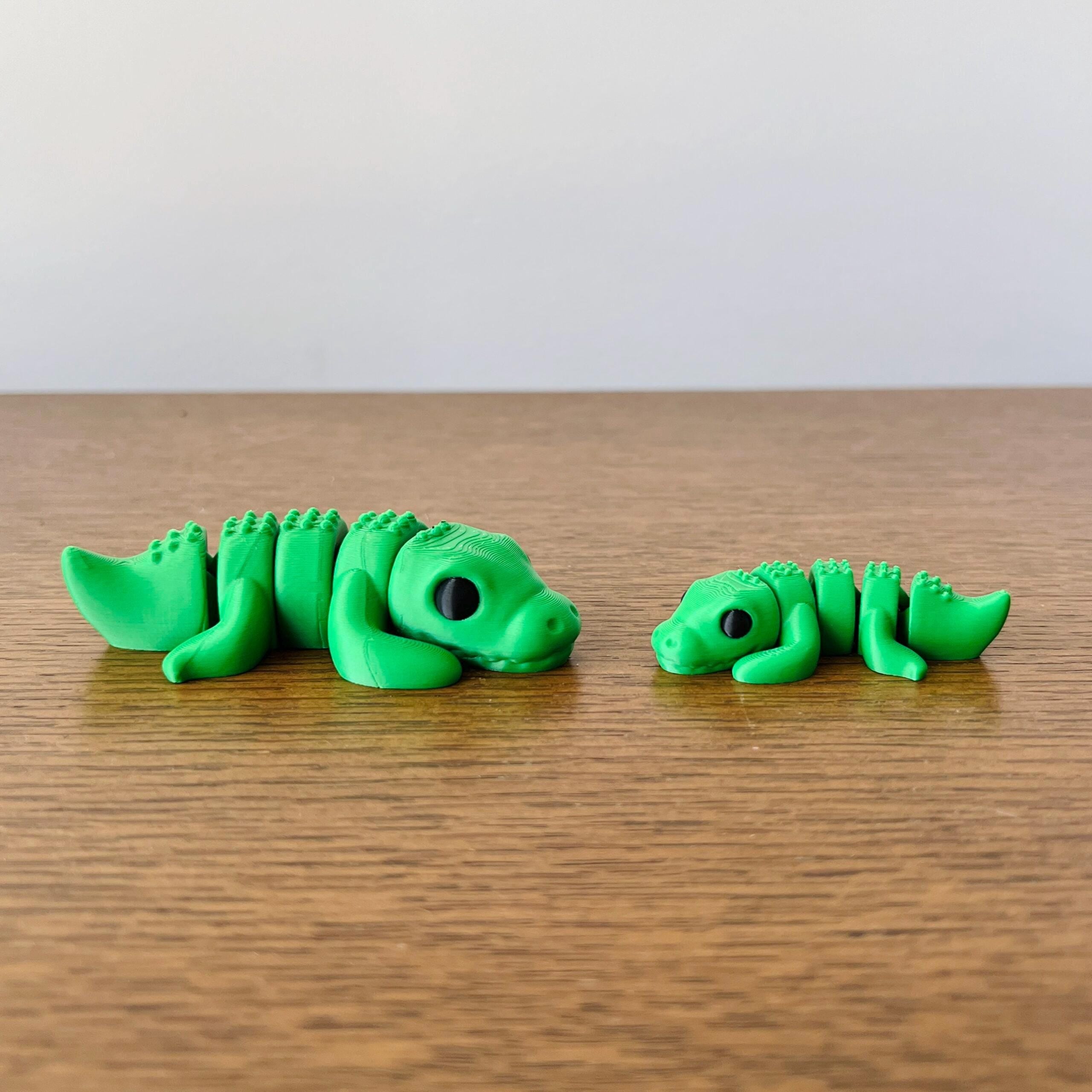 Two vibrant green crocodile figures, one large and one small, resting side by side on a wooden surface.