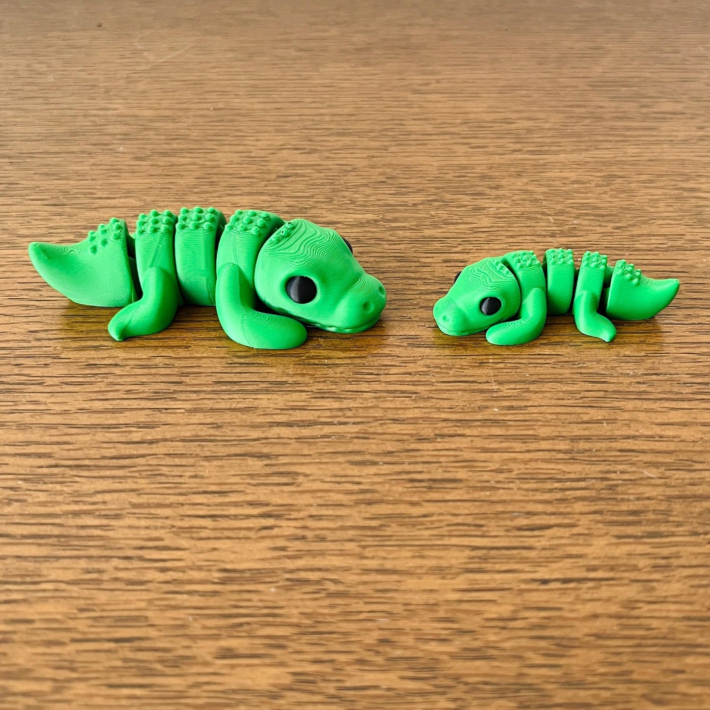 Two playful green crocodile figures, one large and one small, showcasing detailed features on a wooden surface.