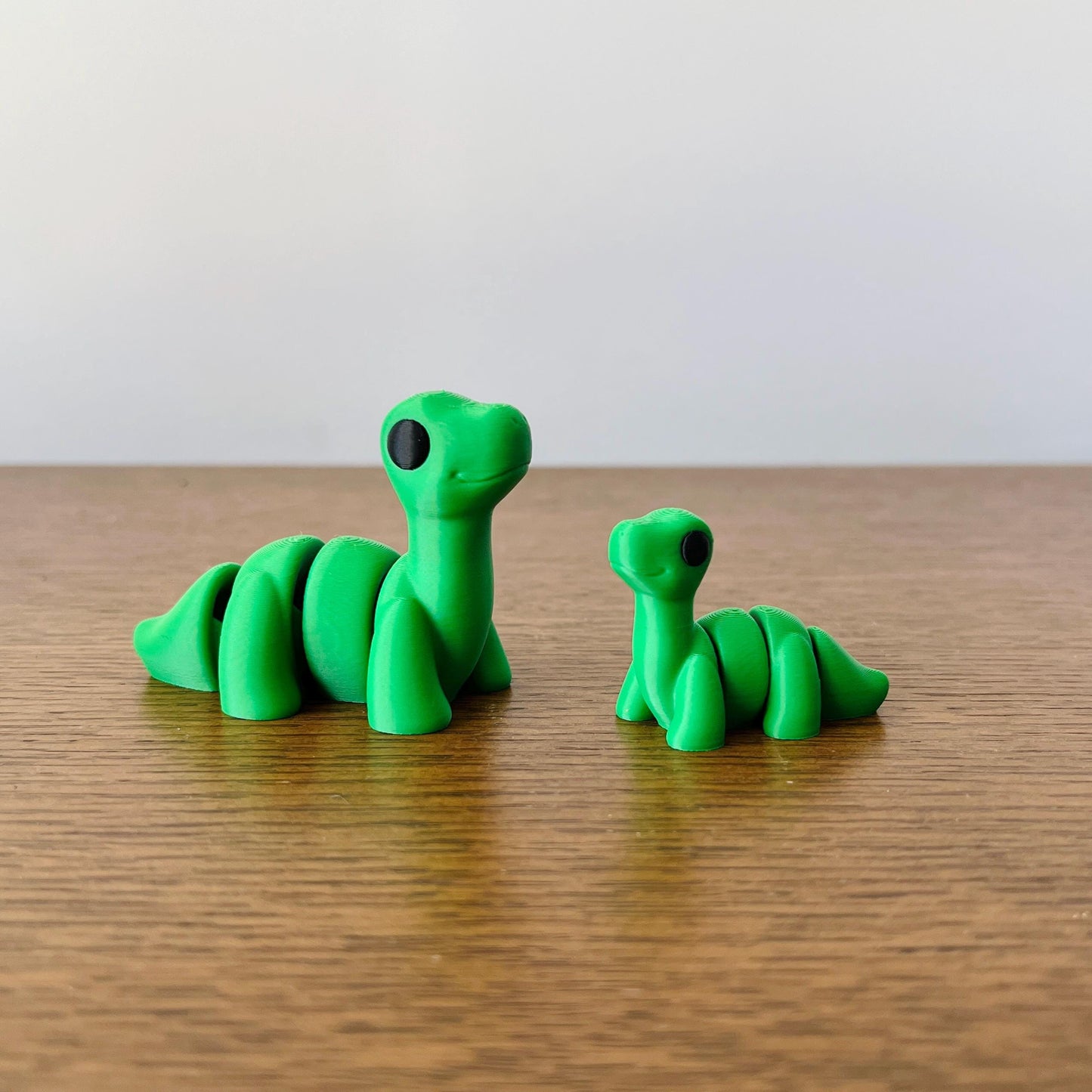 Charming green Brontosaurus figures with large eyes, showcasing intricate details and a classic long-necked shape.