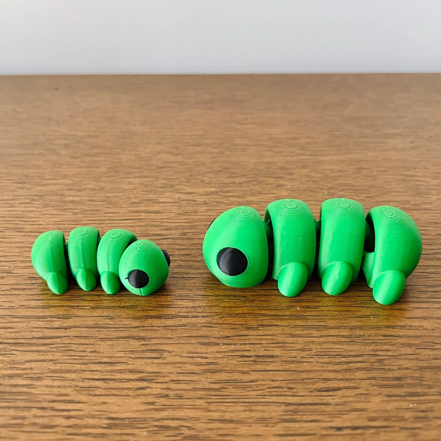 Two playful green caterpillars with black eyes, showcasing whimsical charm on a wooden surface.