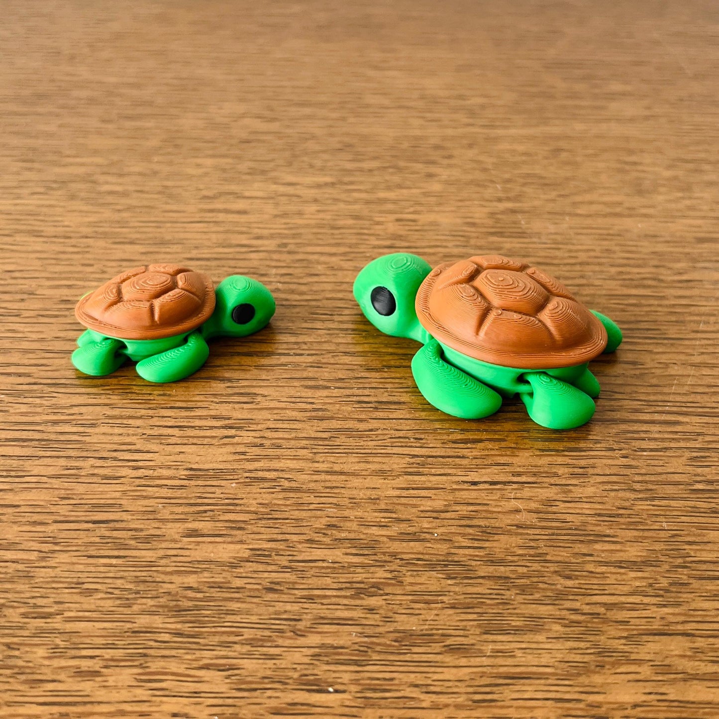Two small green turtles with brown shells, displayed on a wooden surface, showcasing their charming, articulated features.