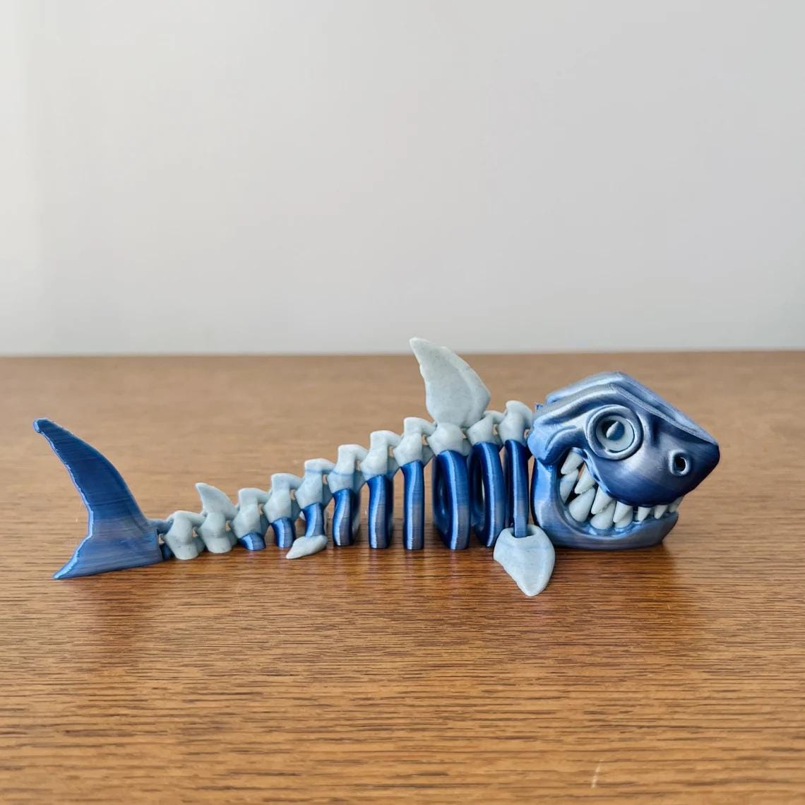 3D-printed skeleton shark figurine in blue tones, showcasing a playful expression and intricate bone details.