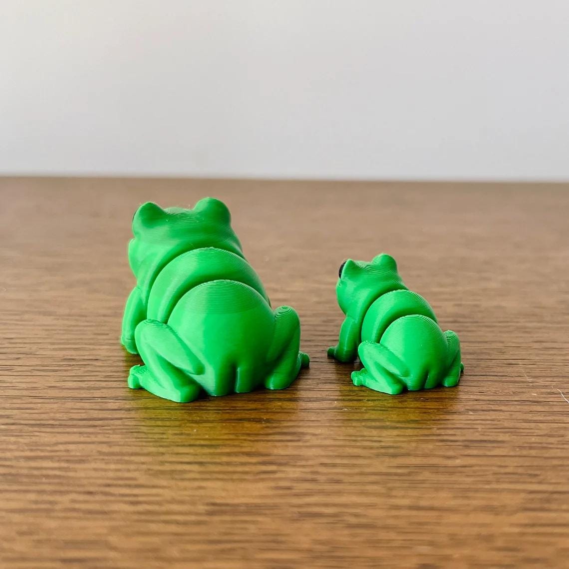 Two vibrant green frogs, one larger and one smaller, showcasing a playful and quirky design on a wooden surface.