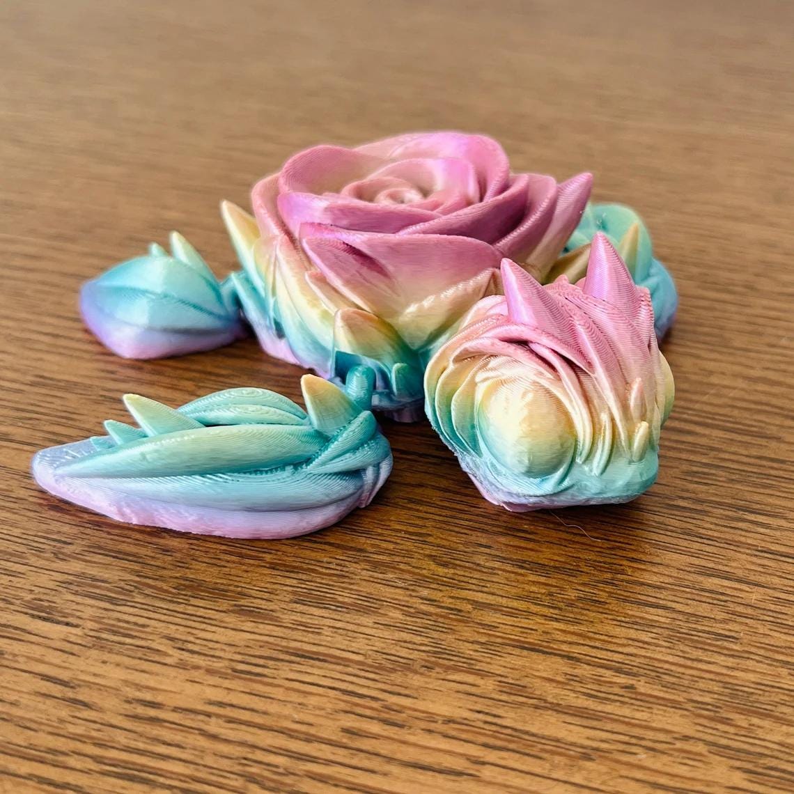 A colorful 3D-printed turtle featuring a pink rose on its back, resting on a wooden surface. Perfect for decor.