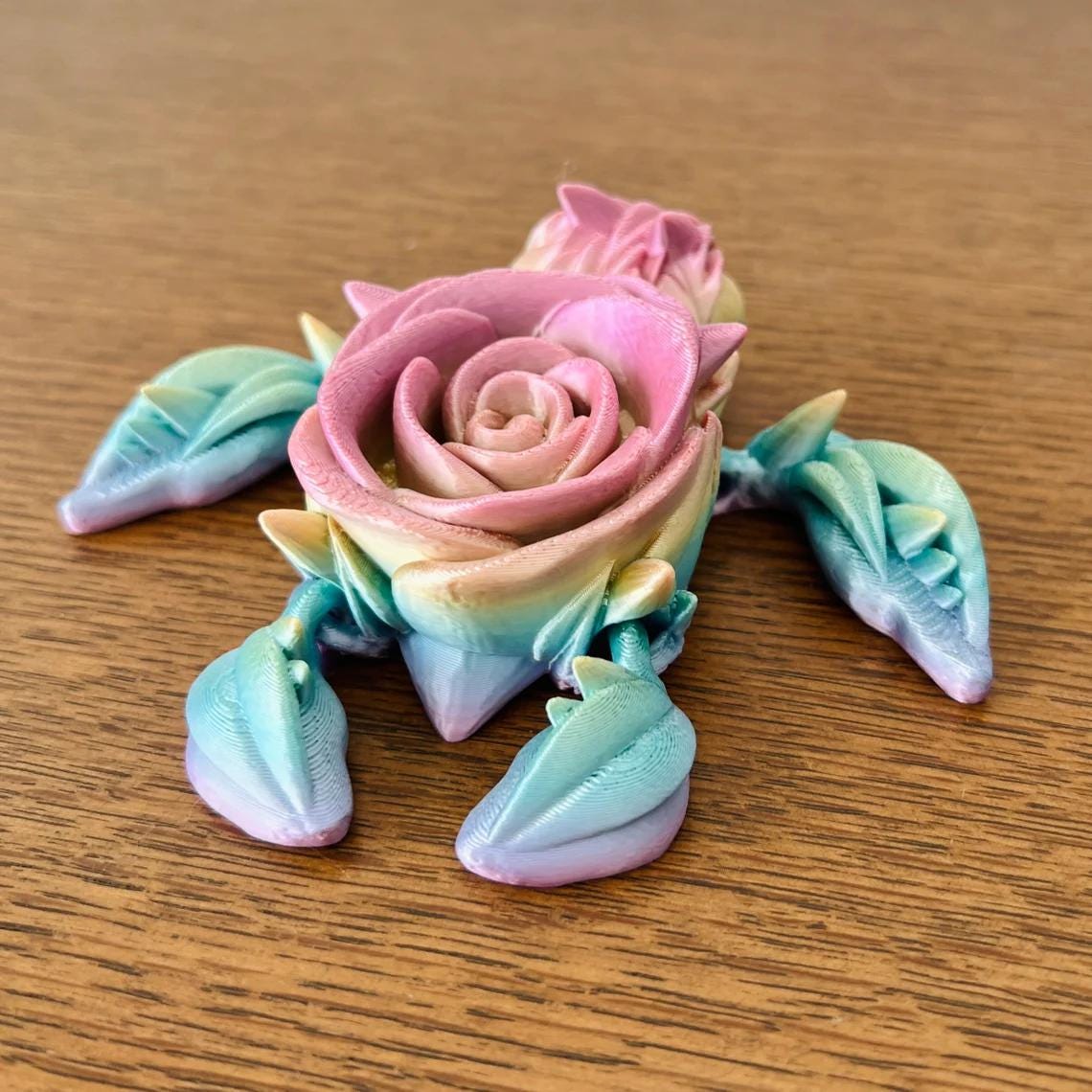 Colorful 3D-printed turtle with a rose flower atop, showcasing soft pink and green hues against a wooden surface.