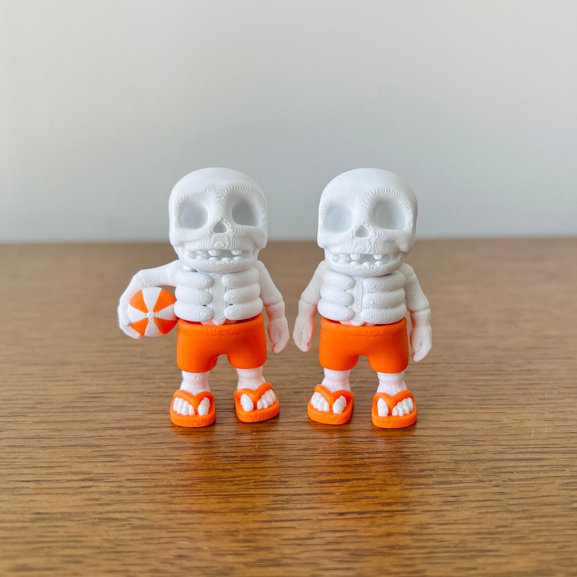 Two 3D printed skeletons in orange shorts and flip-flops, one holding a beach ball, exuding summer fun.