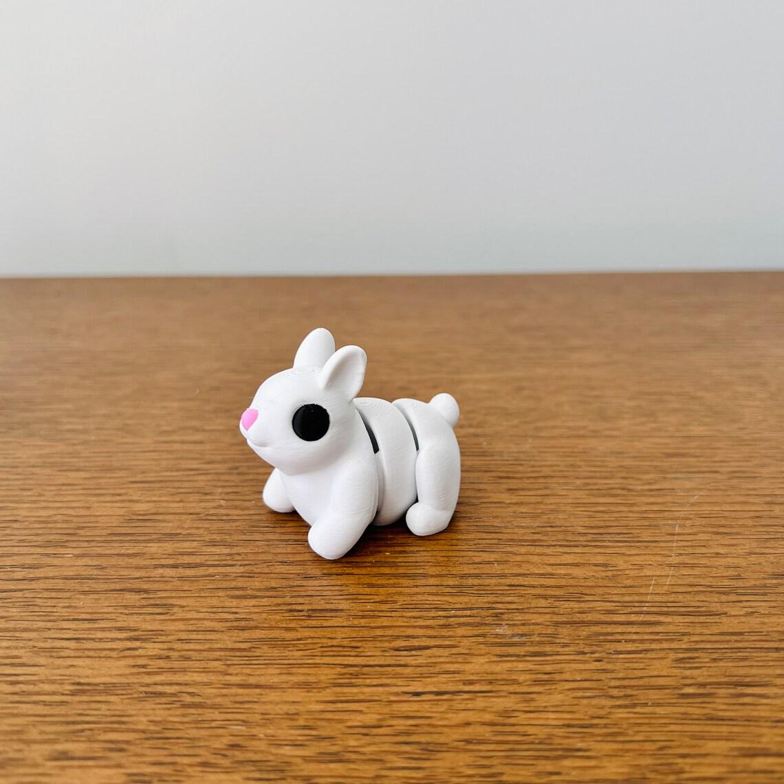 Adorable white bunny with a pink nose and black eyes, featuring articulated joints, resting on a wooden surface.