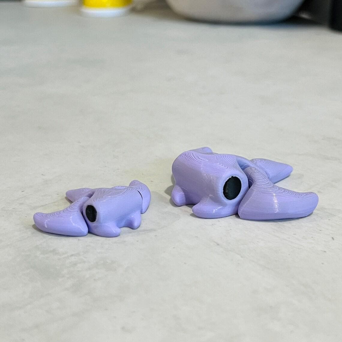 Two purple articulated stingrays, one small and one larger, resting on a smooth surface, emphasizing their playful shapes.