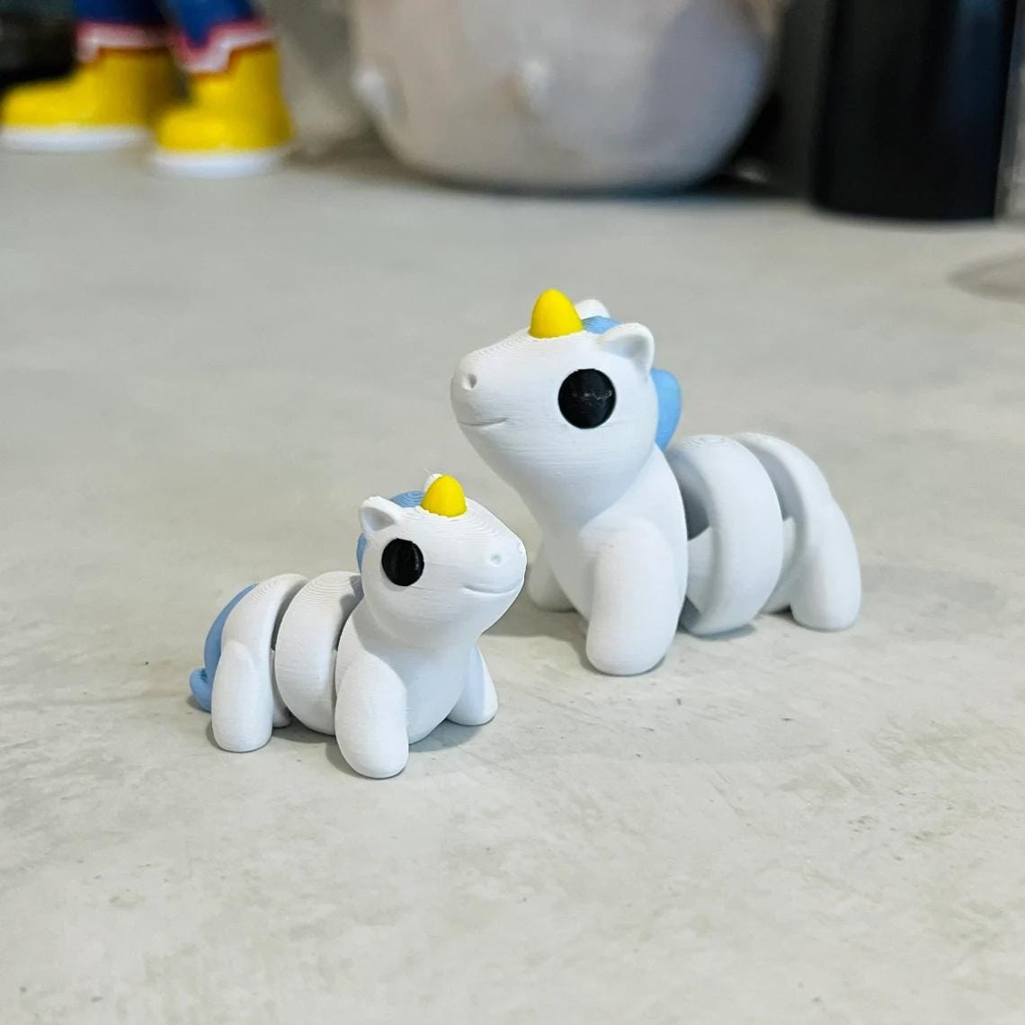 Two adorable 3D printed unicorns in white and blue, featuring articulated bodies and cheerful expressions.