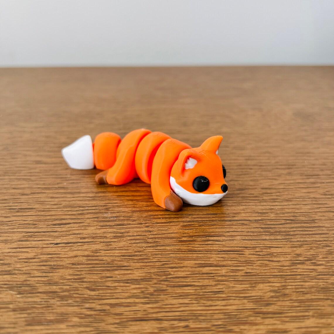Articulated mini fox in vibrant orange and white, perfect for sensory play and stress relief on a wooden surface.
