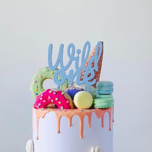 Colorful cake topper reading "Wild one" above vibrant sweets and dripping icing, perfect for a playful celebration.