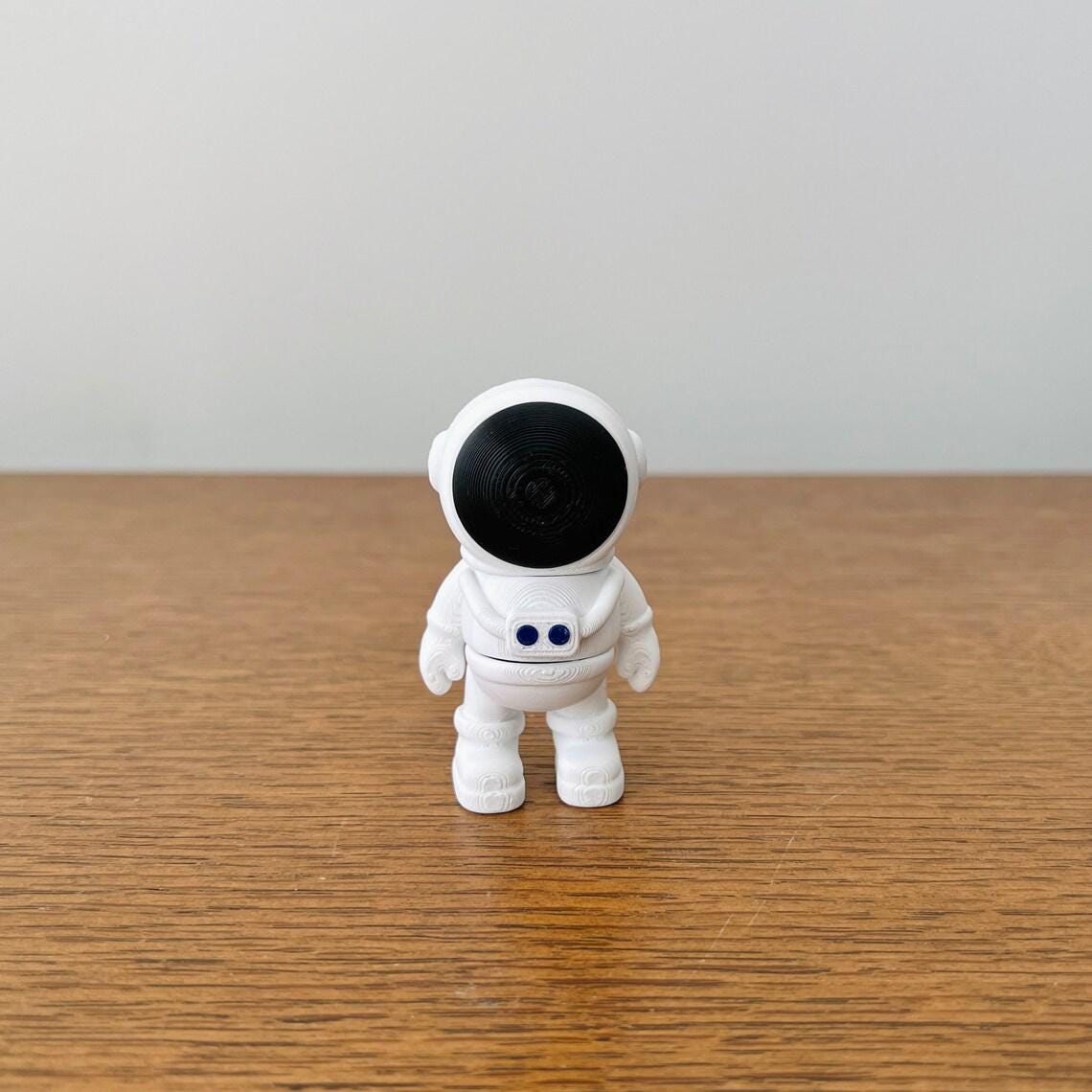 A small white astronaut figure with a black helmet and blue eyes stands on a wooden surface, ready for cosmic adventures.