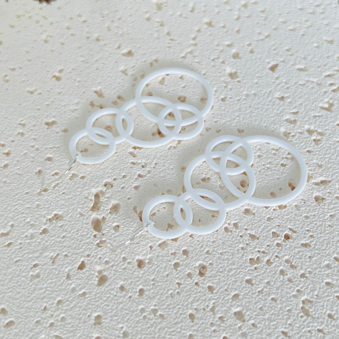 White bubble dangle earrings with multiple circular layers, hanging from sterling silver hooks, on a textured surface.