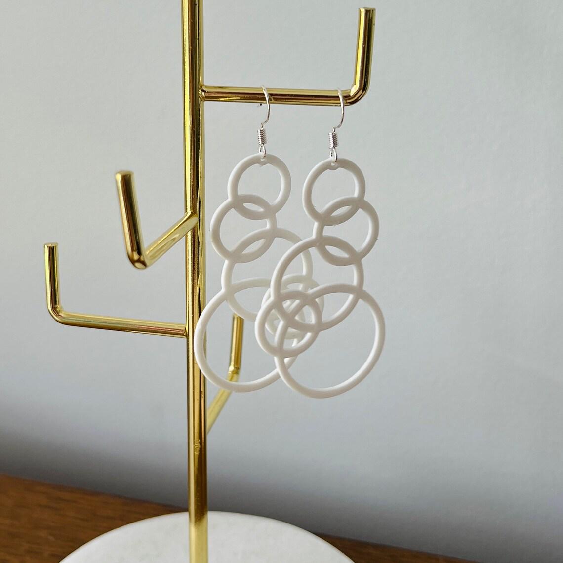 White bubble dangle earrings hang elegantly on a gold display stand, showcasing their playful, modern design.