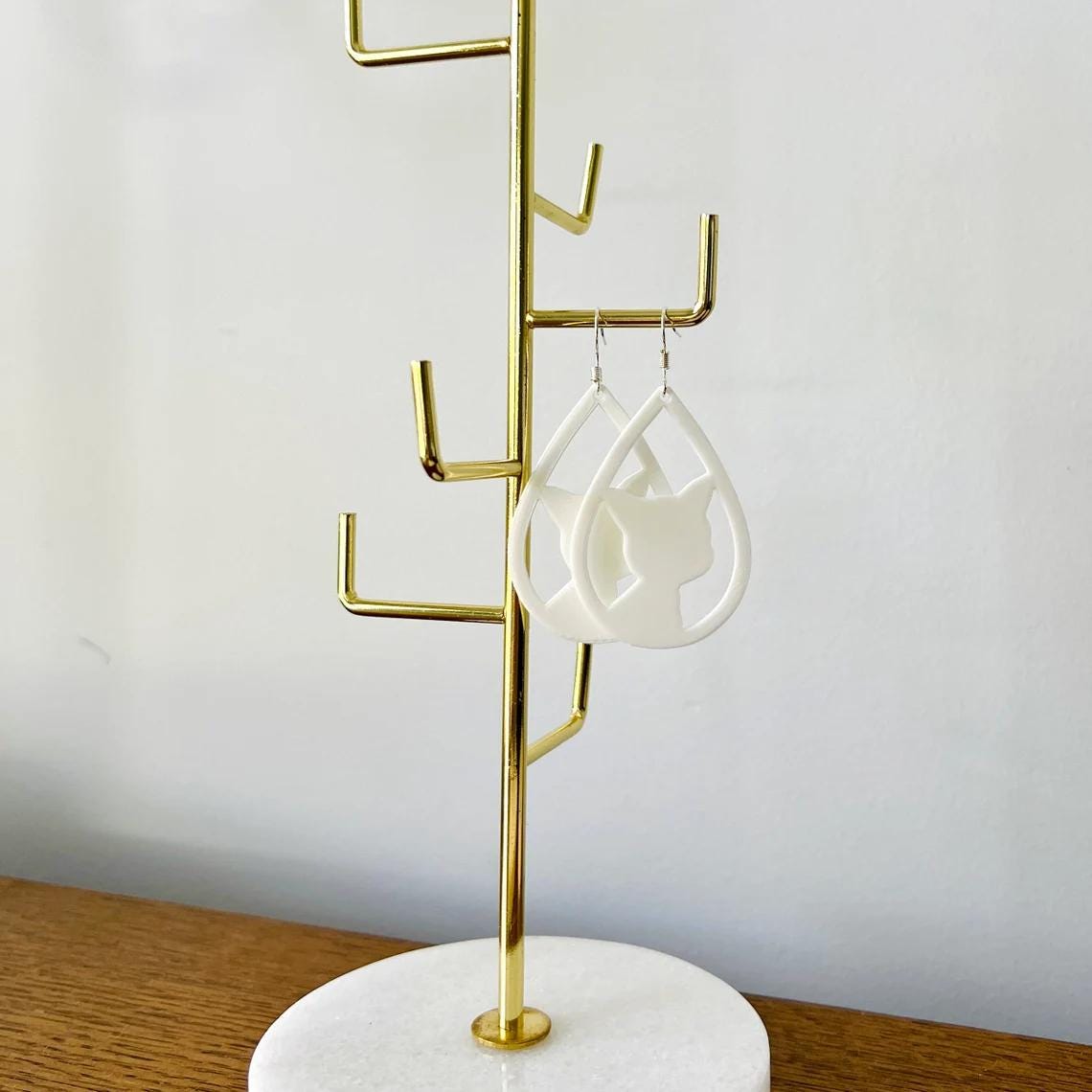 Charming white cat face dangle earrings hanging from sterling silver hooks on a stylish display stand.