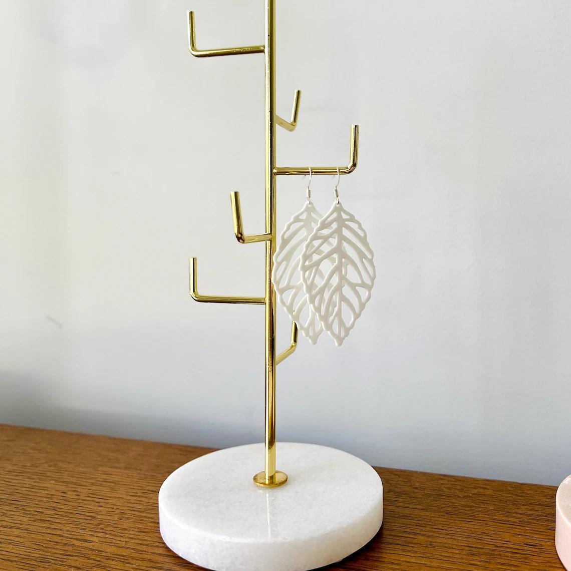 White leaf-shaped dangle earrings hang elegantly on a gold display stand, showcasing their delicate design and lightweight ap