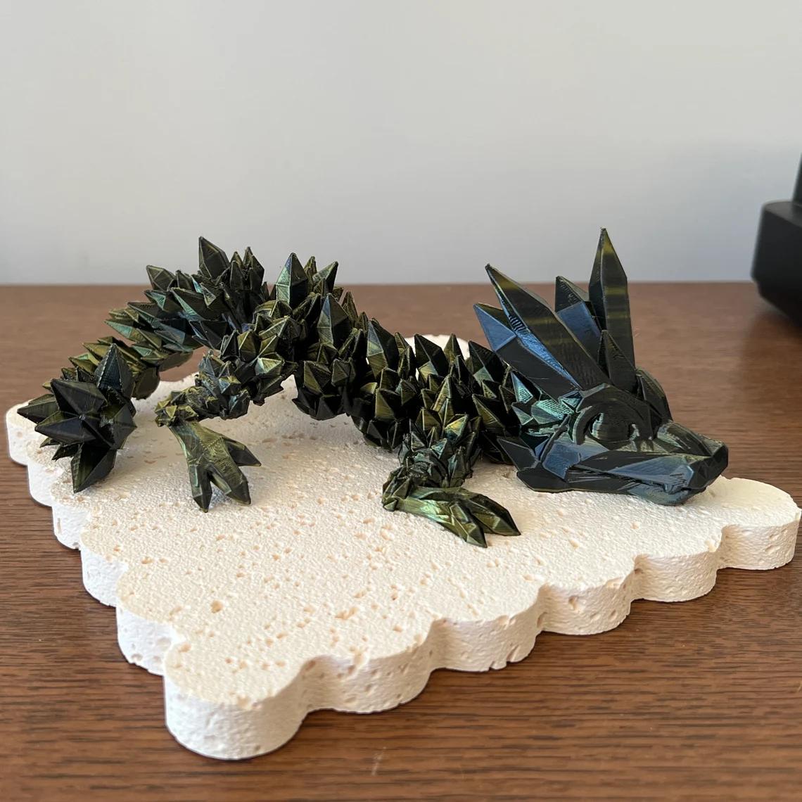 3D printed crystal dragon figurine with vibrant colors and intricate spiked details, resting on a textured base.