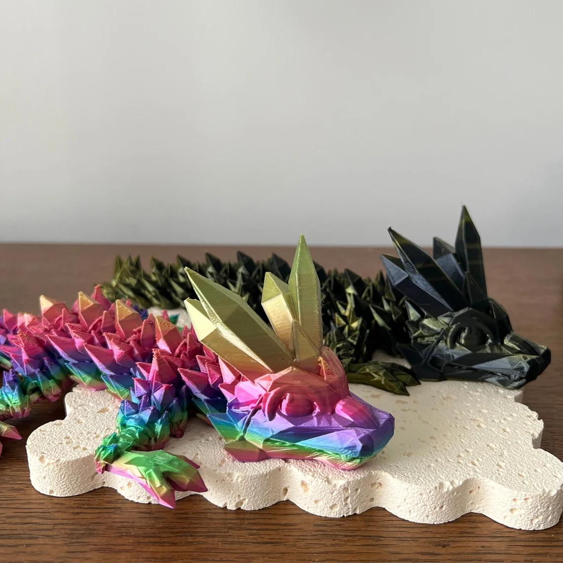 Vibrant 3D-printed dragon figurine in rainbow hues with sharp, golden spikes, resting on a textured base.