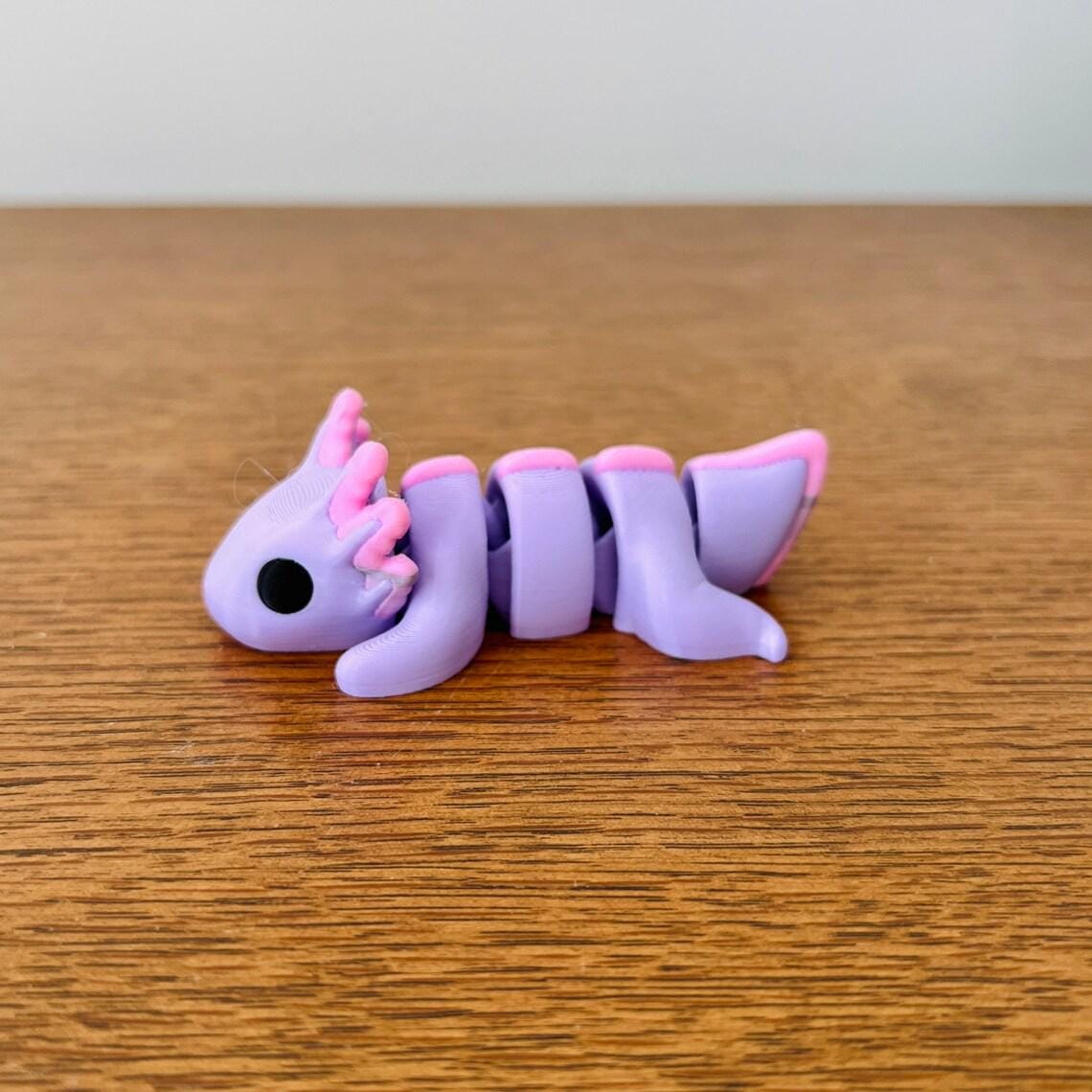 Pastel purple axolotl figure with articulated body and pink accents, resting on a wooden surface. Perfect for sensory play.