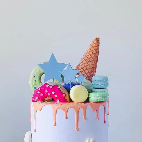 Colorful star toppers adorn a cake, featuring donuts, macarons, and an ice cream cone, creating a whimsical dessert display.