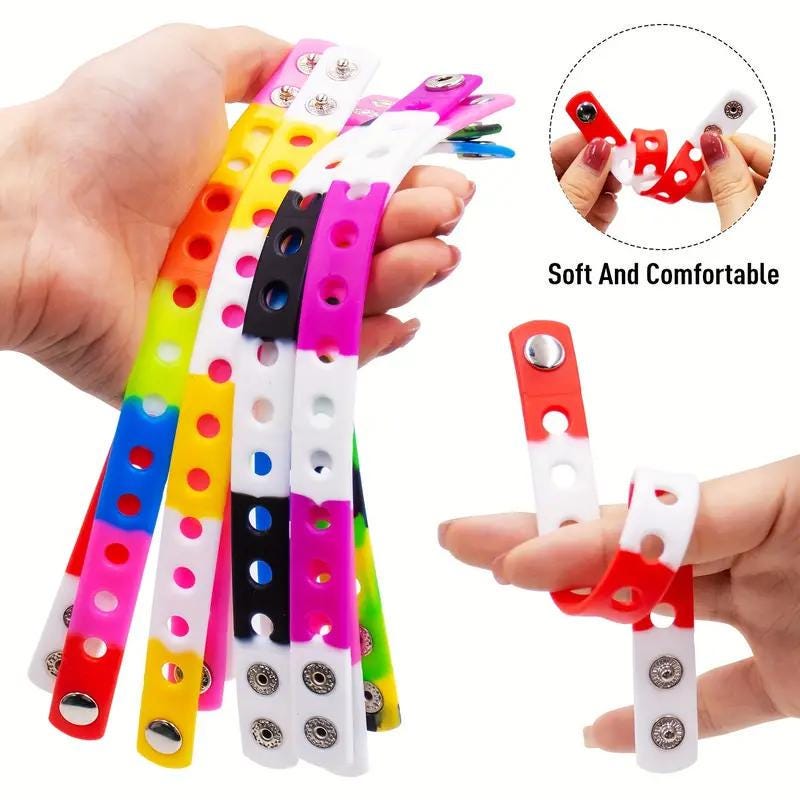 A hand holds colorful silicone charm wristbands, showcasing their flexibility, comfort, and unique snap-button design.