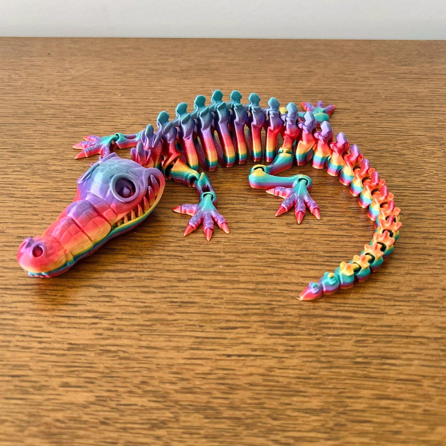 Colorful articulated crocodile figurine featuring intricate details and a striking rainbow pattern on a wooden surface.