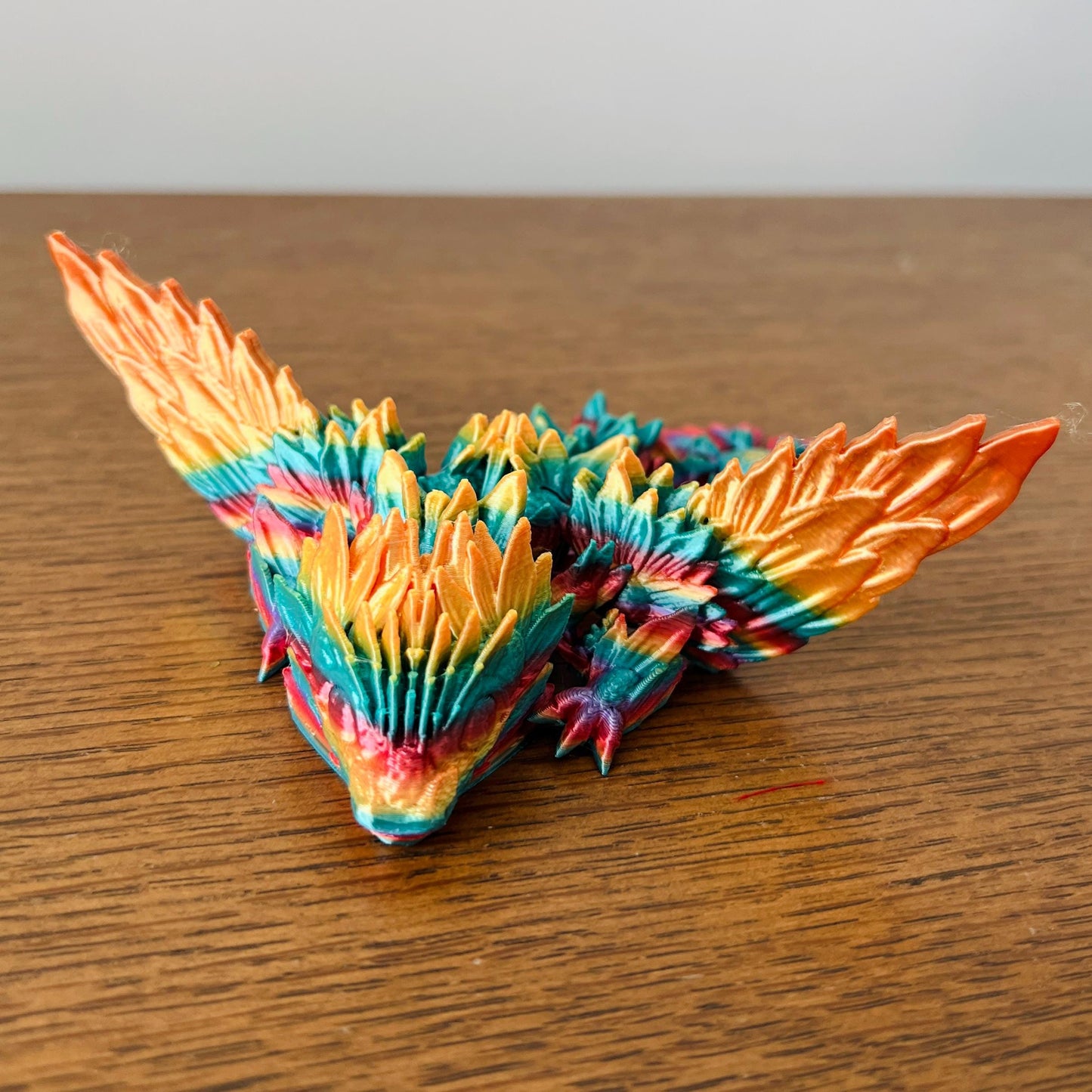 Colorful dragon with vibrant sunflower-inspired wings and detailed textures, resting on a wooden surface.