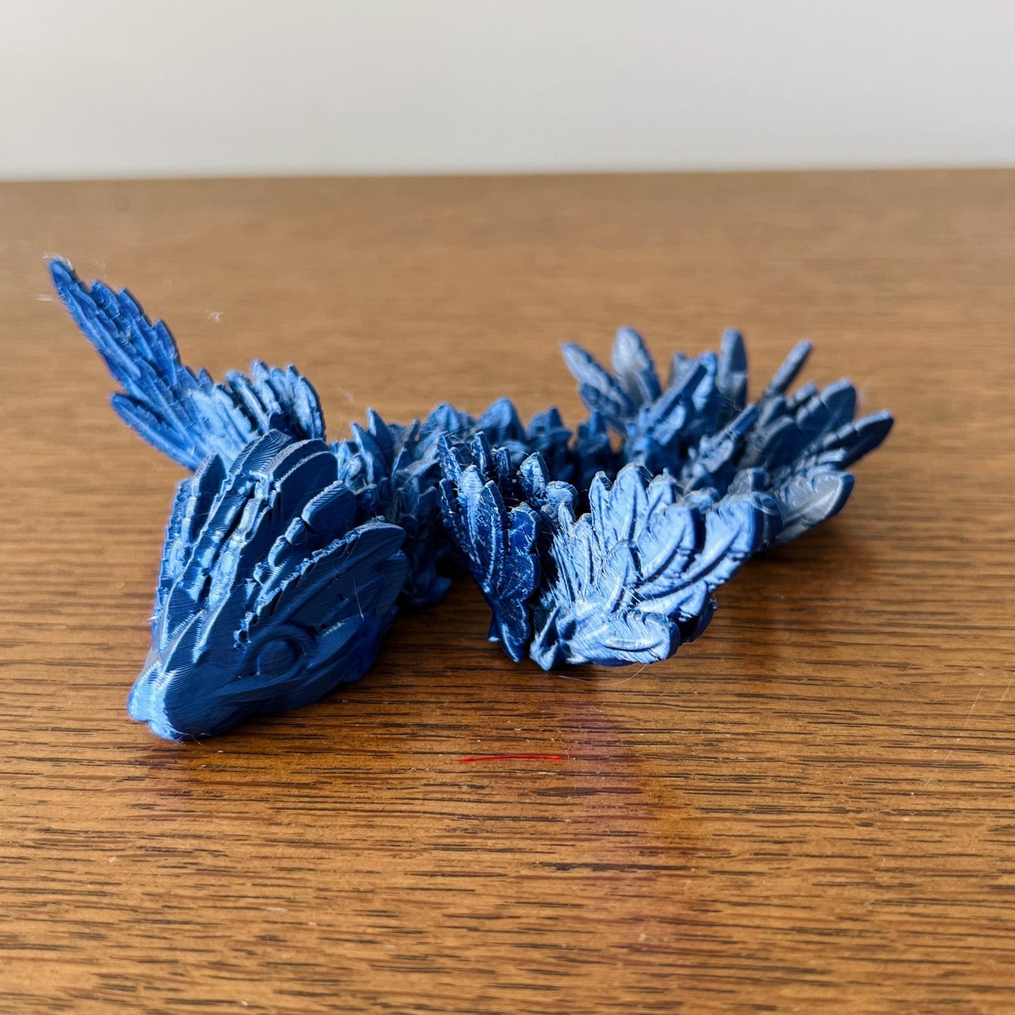 Sleek blue dragon with intricate scales and striking wings, poised gracefully on a wooden surface.