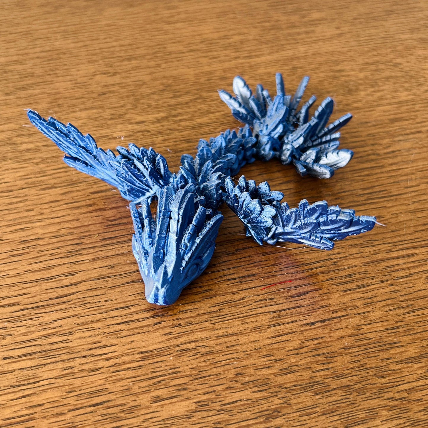 A sleek blue dragon with intricate scales and striking wings, showcasing elegance and power on a wooden surface.
