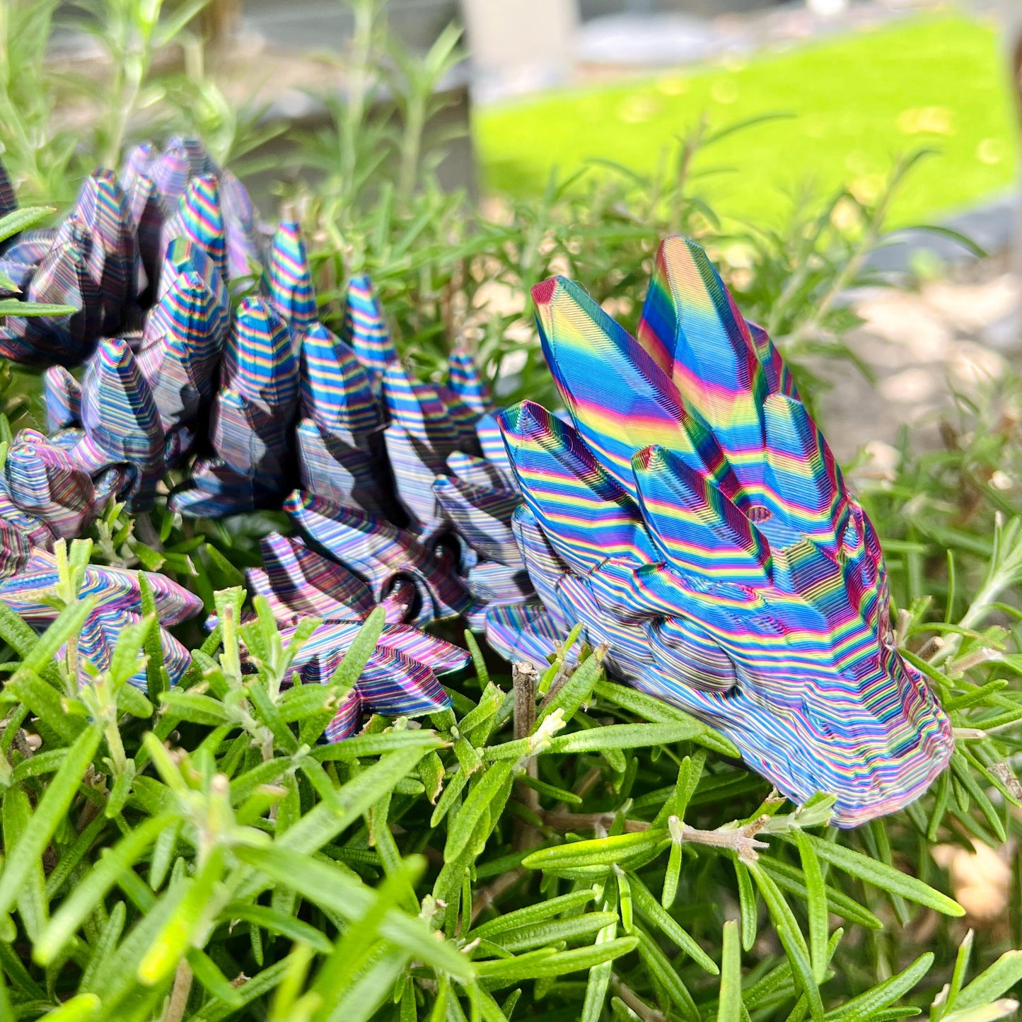 Colorful, intricately detailed dragon with gemstone-like patterns resting among lush green foliage.