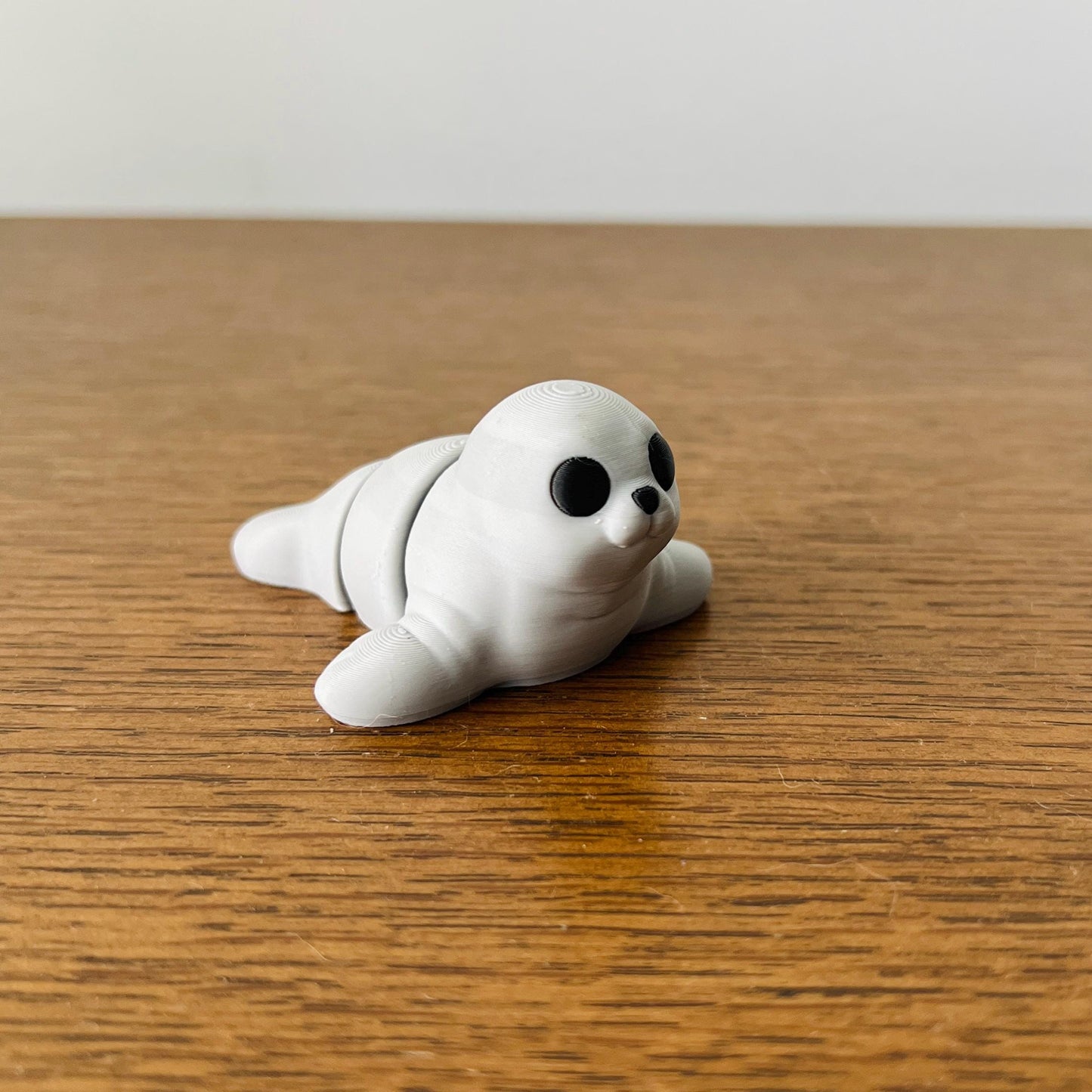 Adorable 3D printed seal with black eyes, lying on a wooden surface, perfect for sensory play and as a charming collectible.