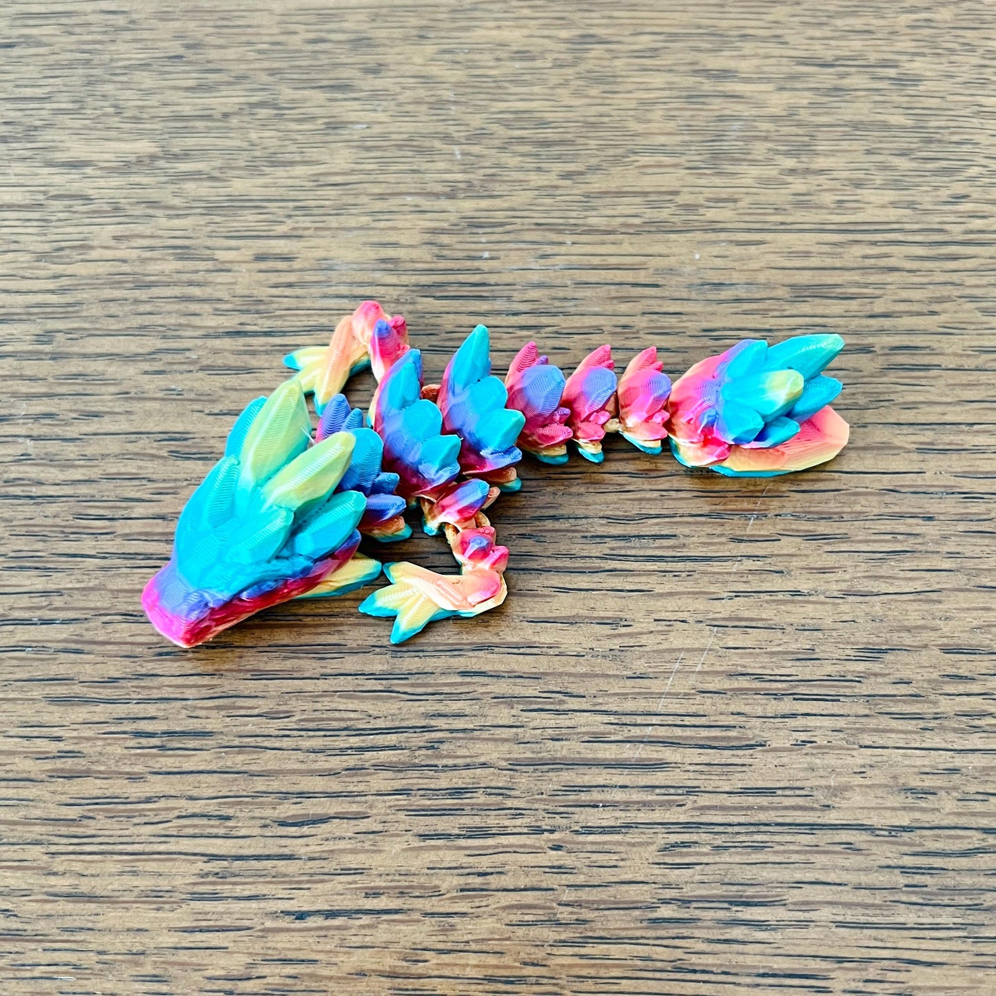 Colorful, articulated mini dragon with gemstone-like details on a wooden surface, perfect for sensory play and collection.