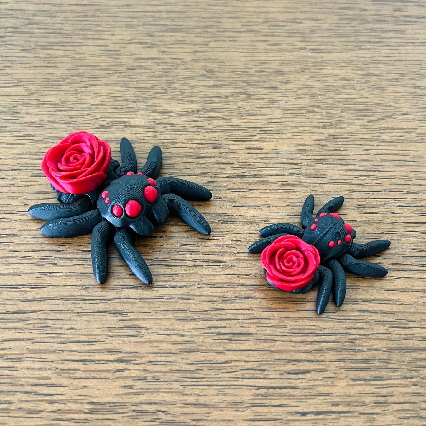 Black spider with red rose detail, showcasing gothic charm and playful elegance, set against a wooden background.