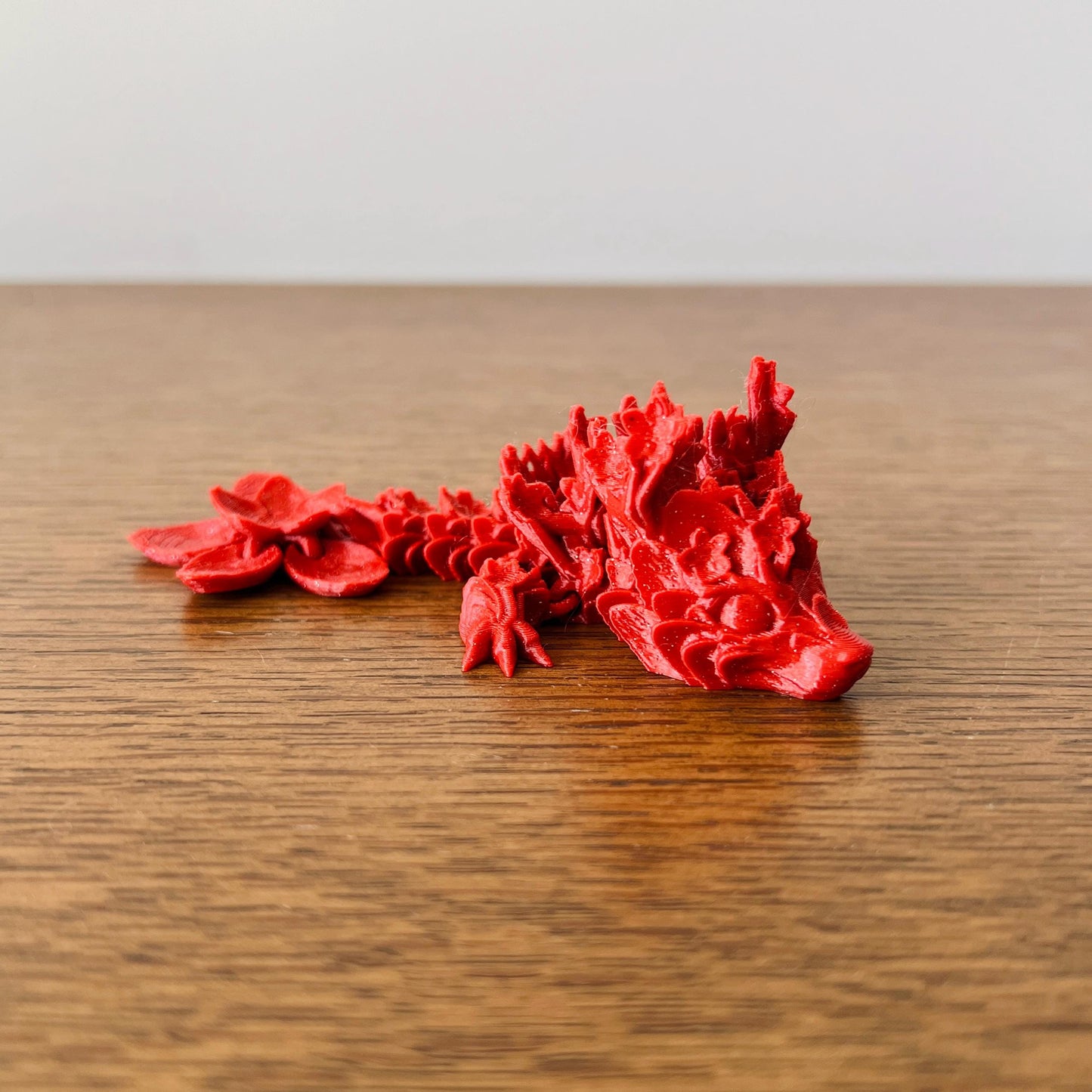 Delicate red dragon resembling cherry blossoms, showcasing intricate floral details, resting on a wooden surface.