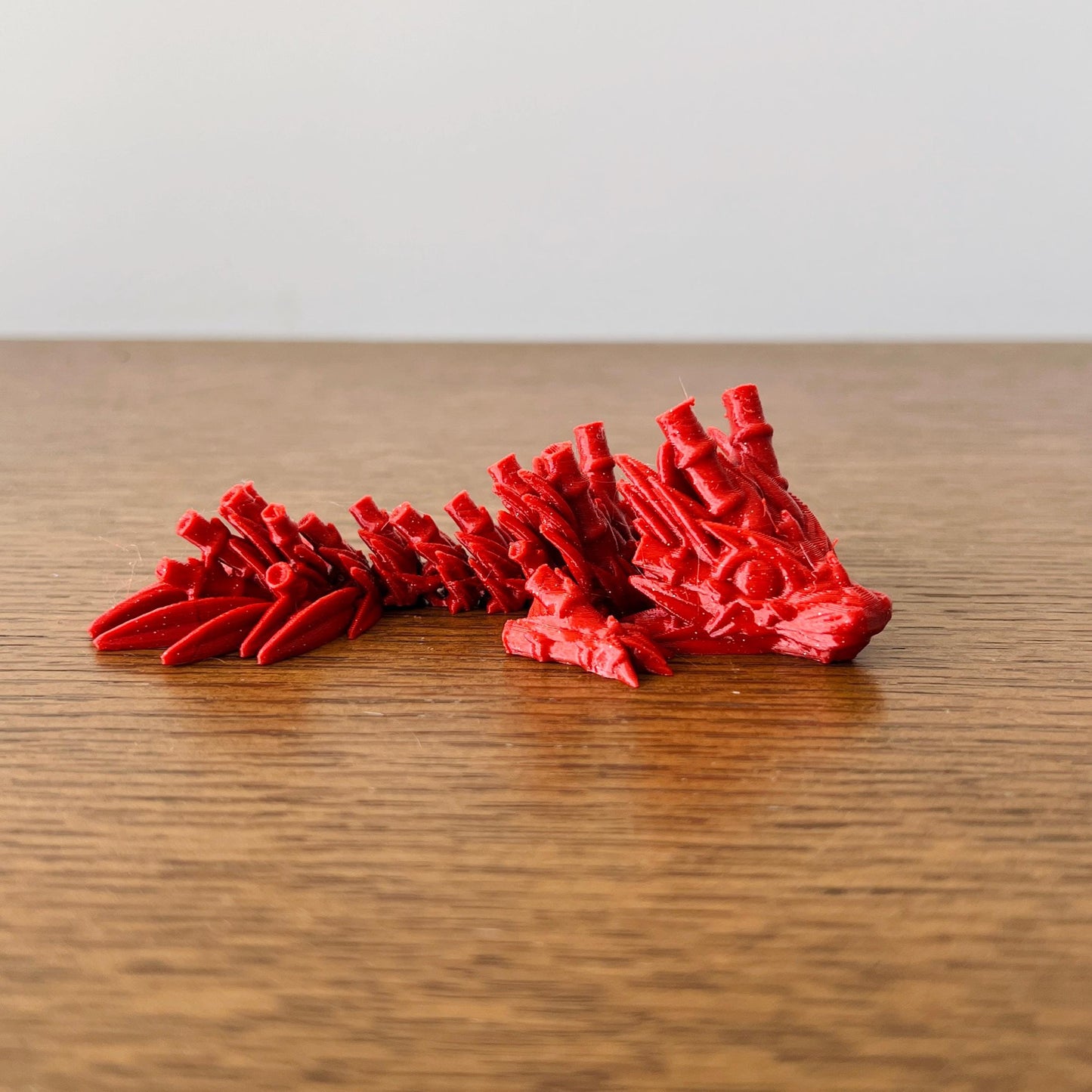 Miniature dragon in vibrant red, detailed with bamboo-like textures, resting on a wooden surface, exuding elegance and streng