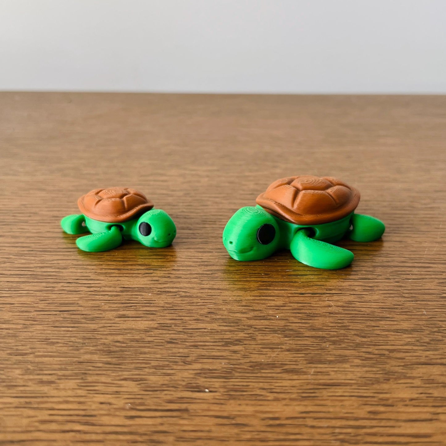 Two cute, articulated green turtles with brown shells sit on a wooden surface, perfect for sensory play or collecting.