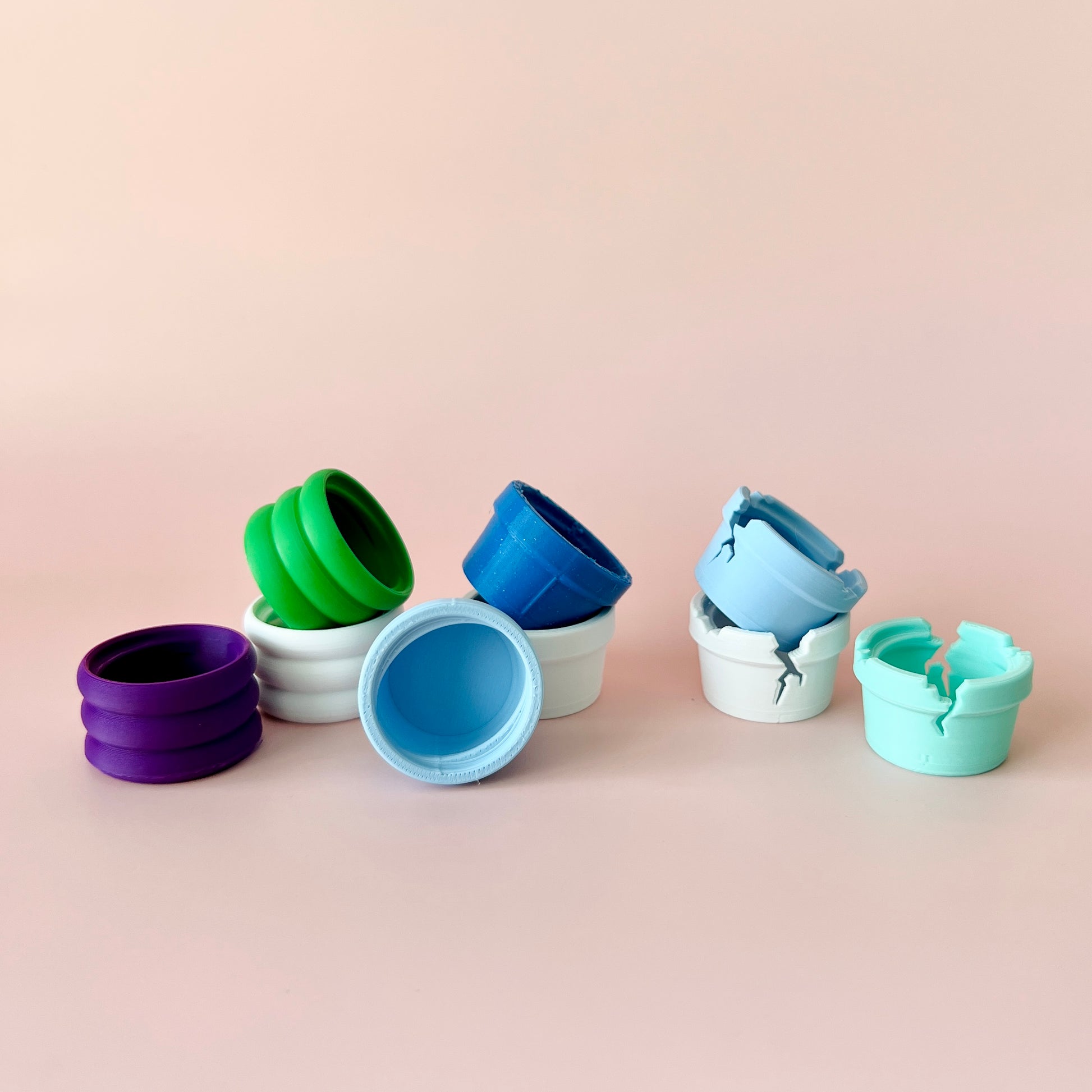 Colorful, cracked and solid containers in various shades arranged playfully on a soft pink background.