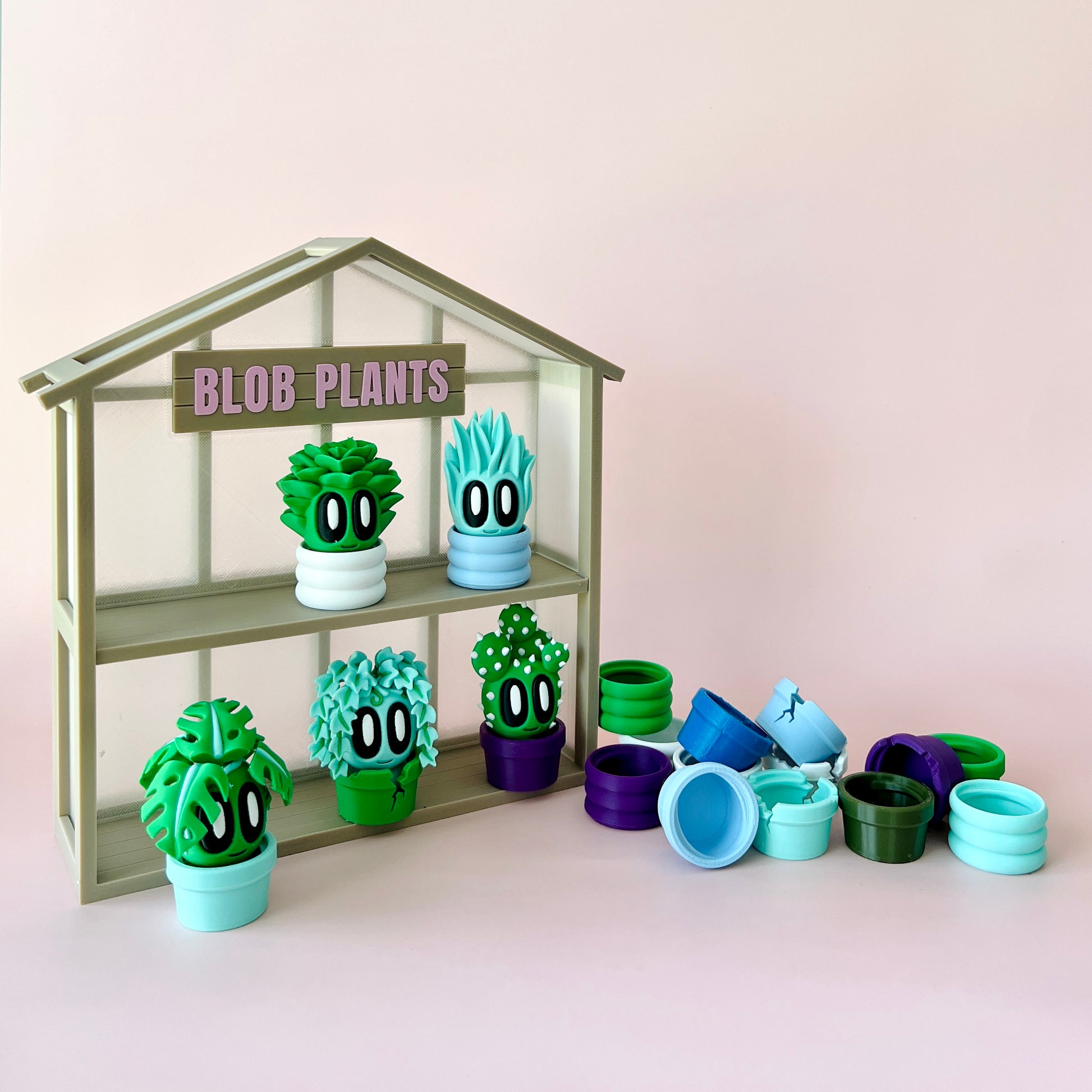 Colorful, whimsical plant figures with large eyes, displayed on a shelf against a soft pink backdrop.