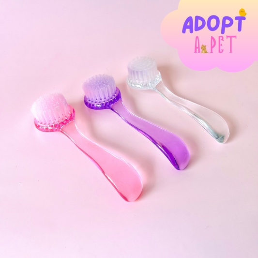 Three colorful brushes with soft bristles on a pink background, featuring shades of pink, purple, and clear.