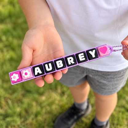 9 Key Fidget Clicker, 3D printed fidget clicker in pink with a personalised name, held outdoors