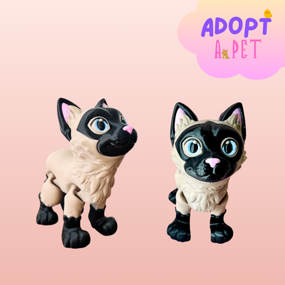 Two playful Siamese cat figurines with bright blue eyes and detailed fur, set against a soft pink background.