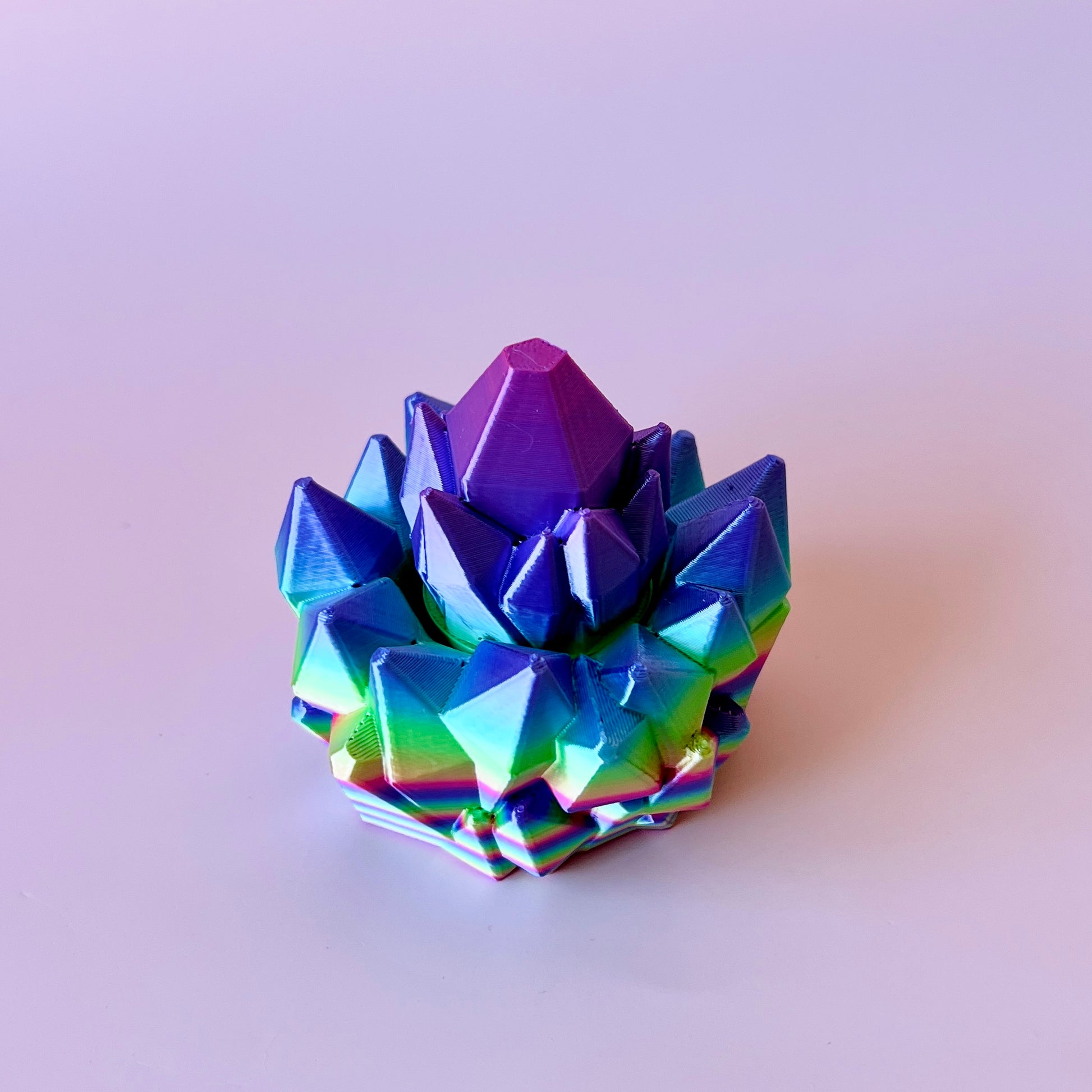 Colorful, multi-faceted crystal-like structure with vibrant purple and green hues, set against a light background.