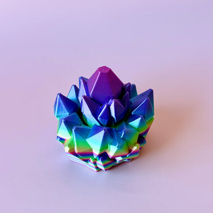 Colorful, multi-faceted crystal-like structure with vibrant purple and green hues, set against a light background.