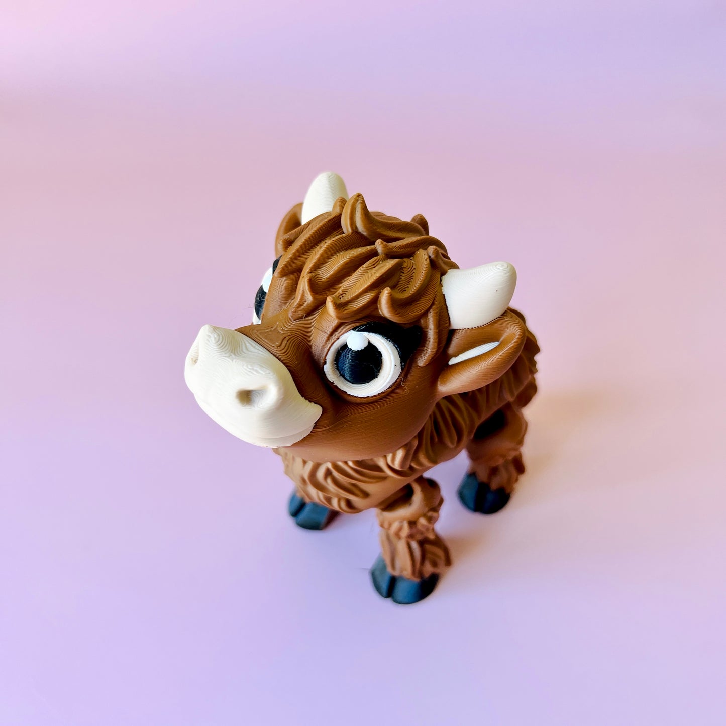 A cute brown Highland calf with big eyes and curly fur, set against a soft pink background.